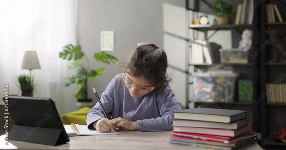 Cute girl studying online, watching internet video course on digital tablet at home, making notes in copybook. Distance learning concept Cute girl studying online, watching internet video course on digital tablet at home, making notes in copybook. Distance learning concept