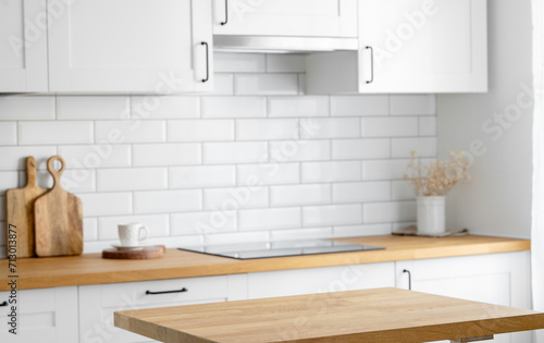 Wooden oak countertop with free space to display or advertise a product or food against a blurred white kitchen with brick background.