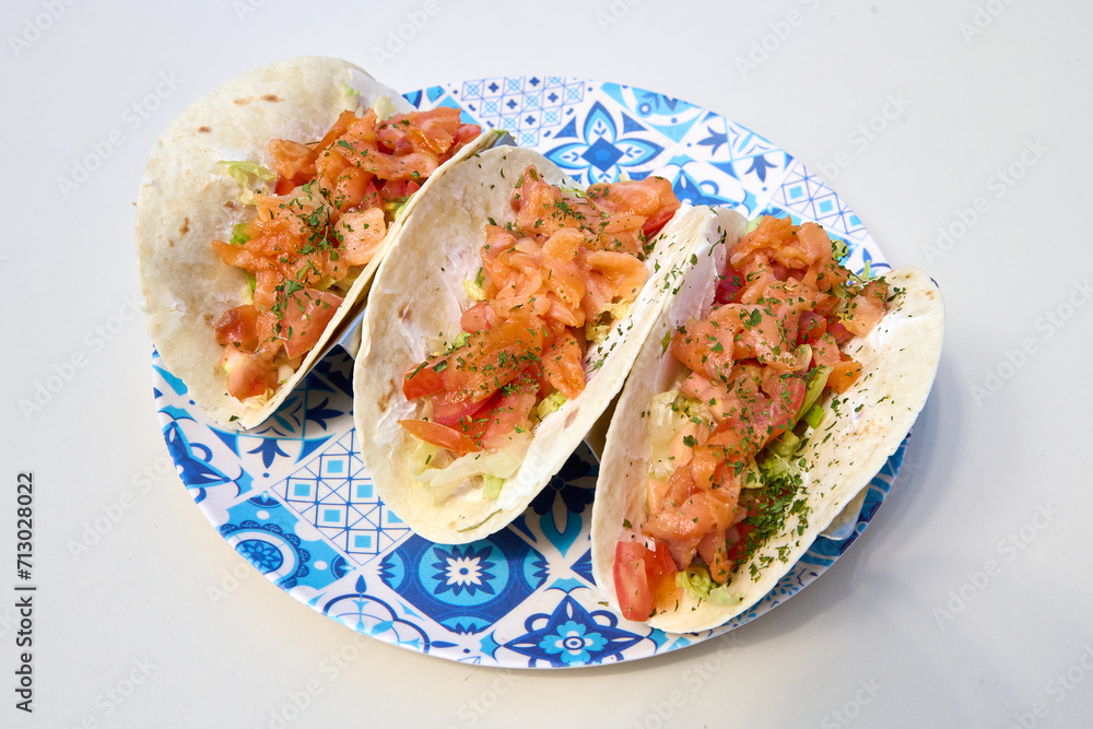 tacos with salmon and tomato on a blue plate on a white background