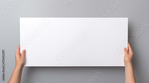 Human hand holding a white board. White blank sheet of paper in hands. Isolated on grey background. Can use for Promotion purpose or Advertising banner. photo