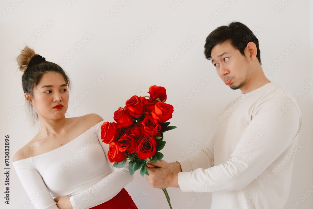 Asian man giving red rosed and flirting, woman bulk dislike and ignoring flowers, both standing isolated over white background wall. Asian man giving red rosed and flirting, woman bulk dislike and ignoring flowers, both standing isolated over white background wall.