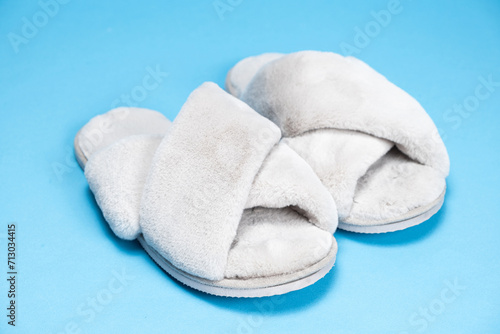 Modern stylish fluffy grey slippers on blue background