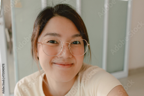 Happy asian Thai woman take selfie and smiling to camera, wearing eyeglasses, relaxing at home. photo