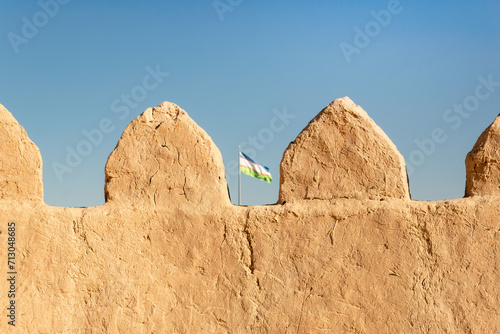 Close-up view city wall of Itchan Kala ancient town at dawn  oriental architecture  wildlife  Khiva  Uzbekistan. Top side of walls of Ichan-Kala fortress and national flag of Uzbekistan over the wall.