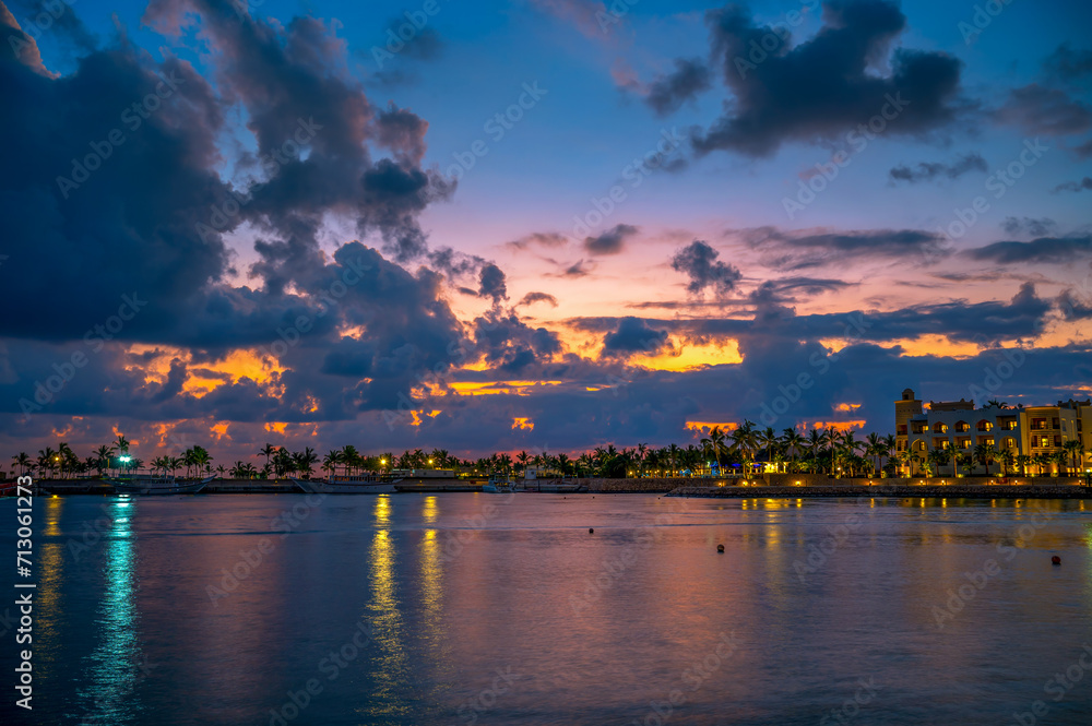 Sunset above coastline in Salalah, Oman, with yachts, clouds and palm trees. Salalah is a vibrant city known for its lush, tropical landscape and rich cultural heritage in the southern region of Oman.