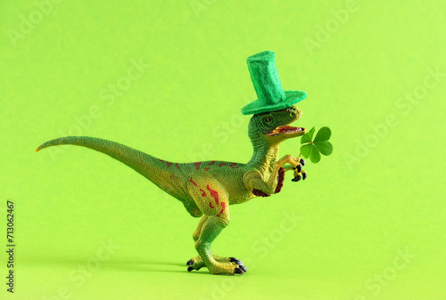 Green dinosaur in green hat holds leaf of clover. Wide banner. Copy space. © dvulikaia