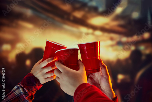 Group of friends meeting, clicking disposable plastic red cups over blurred background. Concept of holidays, celebration, events, friendship, leisure activity photo
