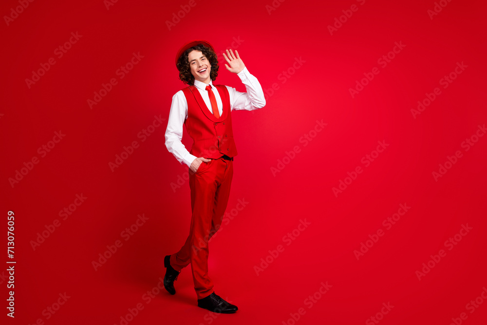 Full body photo of friendly in retro clothing boy wearing vest and shirt waving arm at new year event isolated on red color background