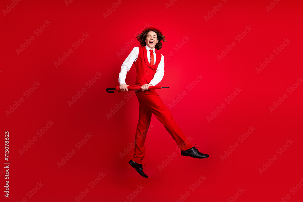 Full length photo of funky guy in stylish outfit jumping and moves with parasol and dance boogie woogie isolated on red color background