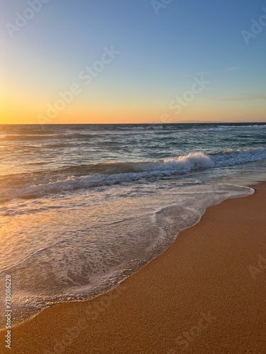 Warm colors of the seascape, sand sea coastline, sea waves on the sand, clear blue sky, no people, empty beach