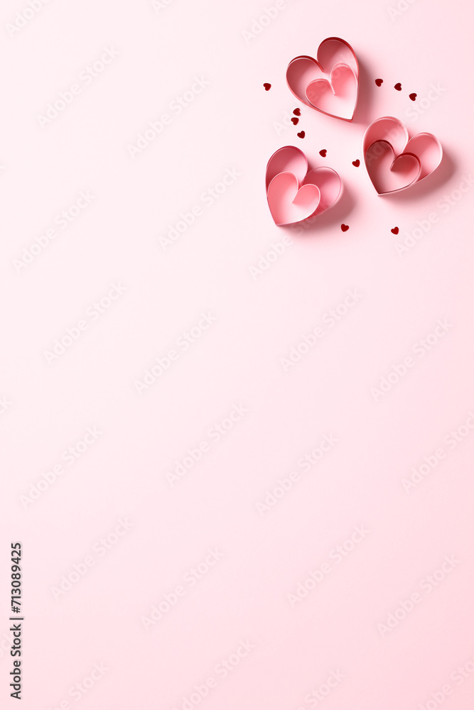 Top view photo of Valentine's Day red paper cut hearts decorations on pink table. Flat lay, overhead.