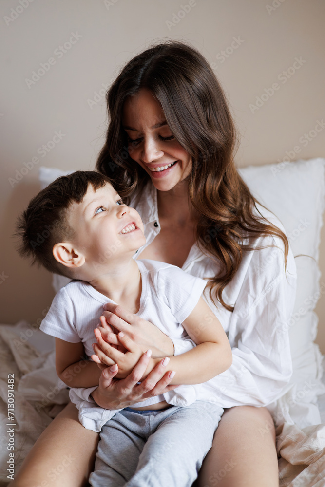 Smiling young mother hugging toddler son in pajama on bed at home Smiling young mother hugging toddler son in pajama on bed at home