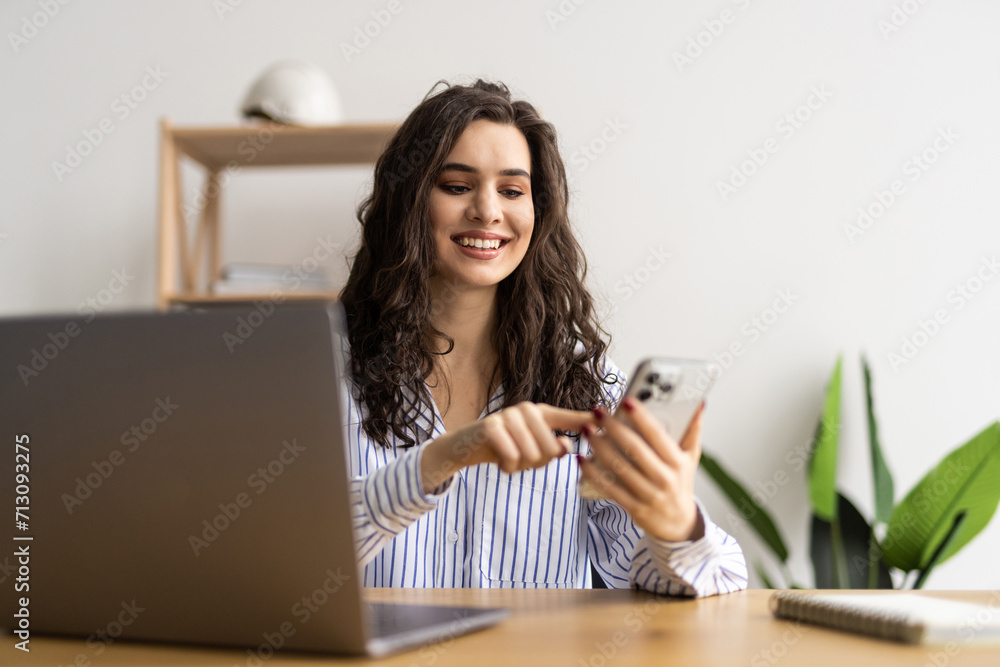 Young smiling business woman sitting at table in coffee shop and uses smartphone. Young smiling business woman sitting at table in coffee shop and uses smartphone.