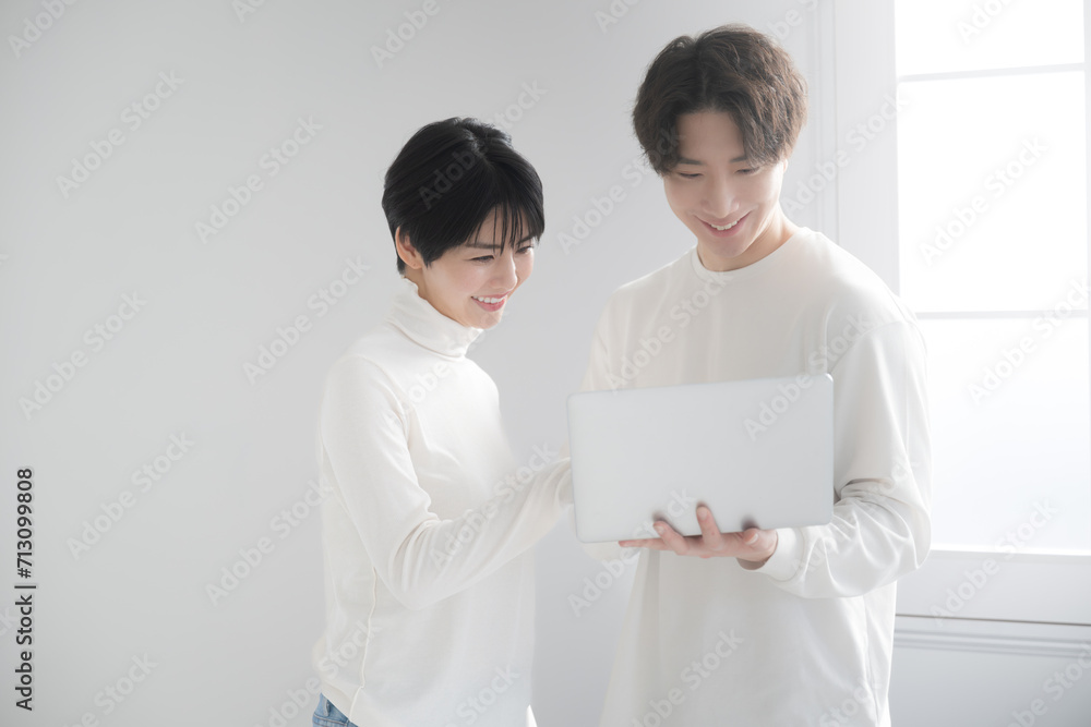 Fresh Asian (Japanese) couple looking at computers on the web together in a bright white room. Moving, house hunting and searching for rentals. Fresh Asian (Japanese) couple looking at computers on the web together in a bright white room. Moving, house hunting and searching for rentals.