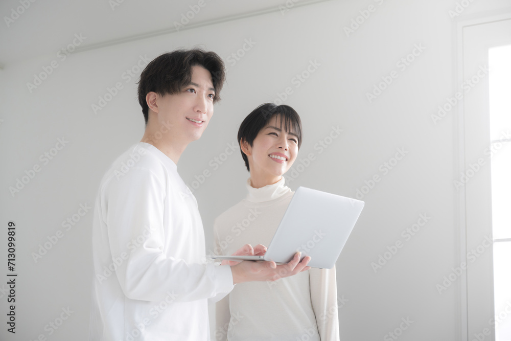 Fresh Asian (Japanese) looking up couple looking at a computer on the web together in a bright white room Moving, house hunting and searching for rentals. Fresh Asian (Japanese) looking up couple looking at a computer on the web together in a bright white room Moving, house hunting and searching for rentals.