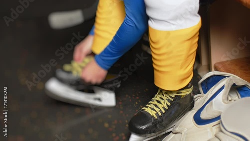 Ice hockey player ties the laces on his skates in locker room before a game, close up. Cloakroom. Male teen get dressed, puts on his sports uniforms, tracksuit in dressing room. Preparing for the game photo