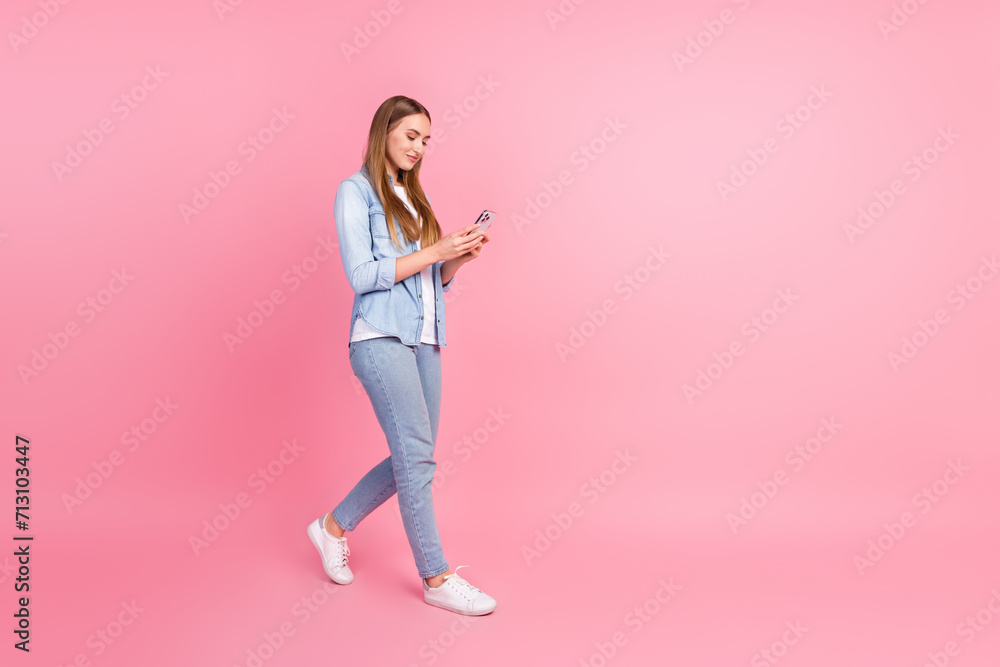 Full length photo of lovely young lady hold gadget walking step eshopping wear trendy jeans garment isolated on pink color background Full length photo of lovely young lady hold gadget walking step eshopping wear trendy jeans garment isolated on pink color background