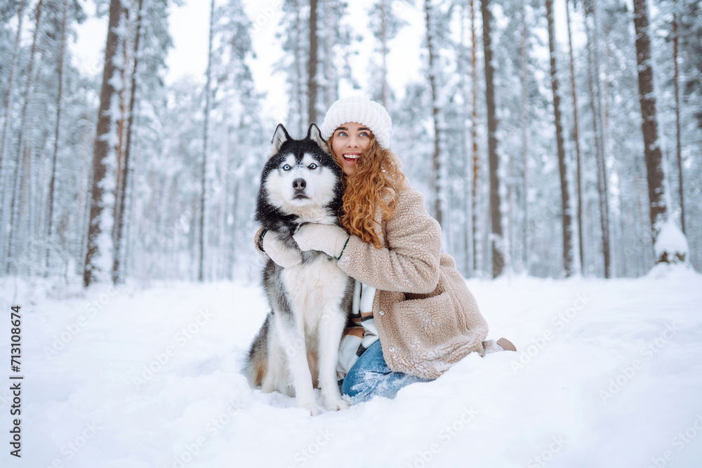 A young woman in warm clothes walking her dog in a picturesque snowy forest. Woman laughing and playing with pet in the park. Domestic dog concept. A young woman in warm clothes walking her dog in a picturesque snowy forest. Woman laughing and playing with pet in the park. Domestic dog concept.