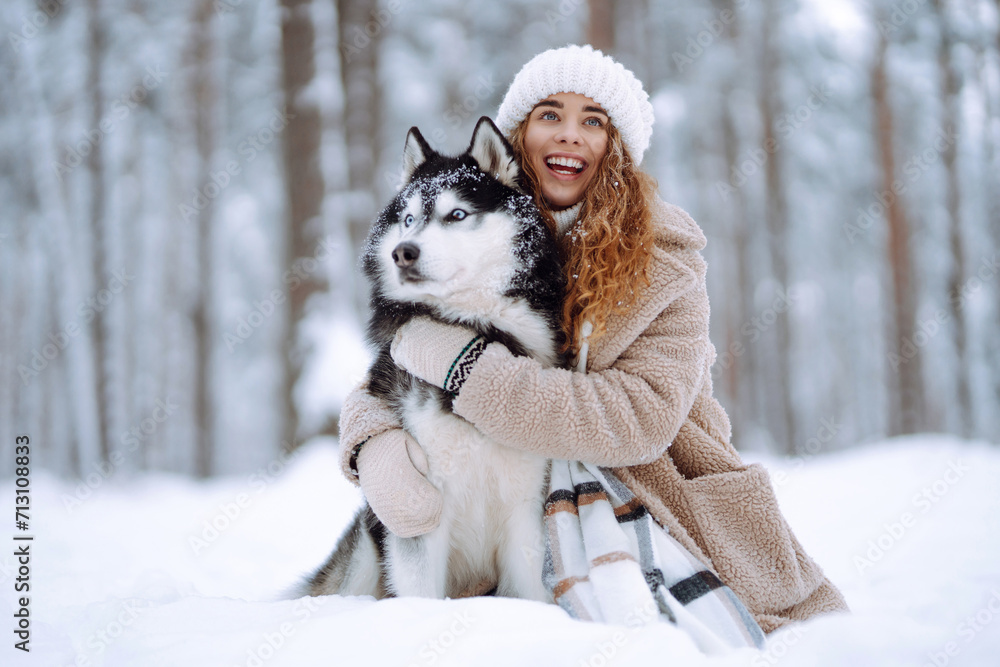 A young woman in warm clothes walking her dog in a picturesque snowy forest. Woman laughing and playing with pet in the park. Domestic dog concept. A young woman in warm clothes walking her dog in a picturesque snowy forest. Woman laughing and playing with pet in the park. Domestic dog concept.