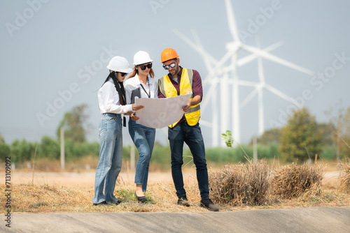 Group of engineers and architects on construction site with wind turbines in background