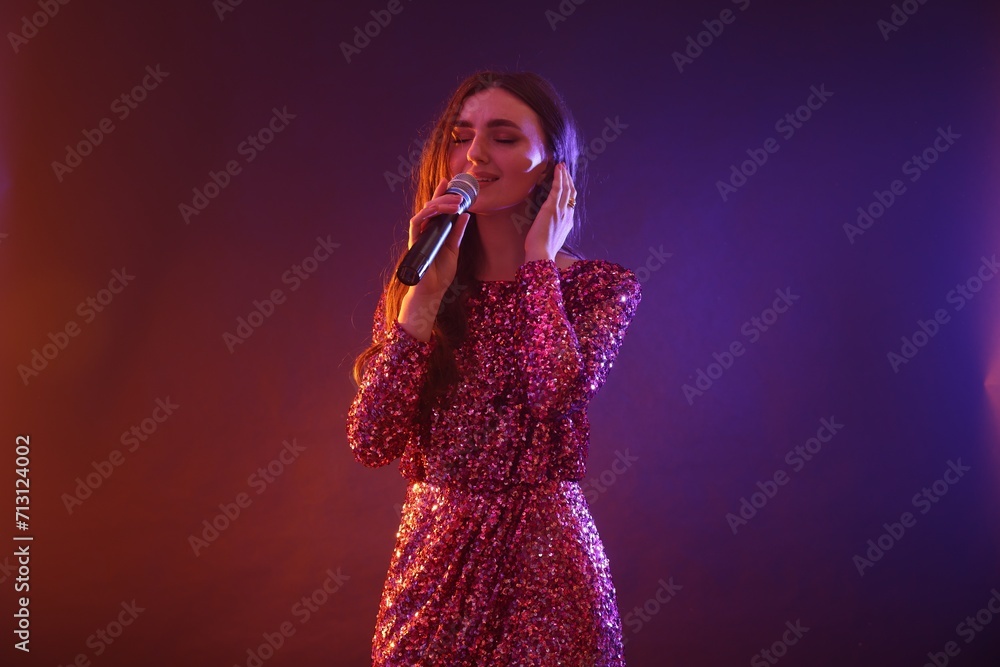 Emotional woman with microphone singing on bright background