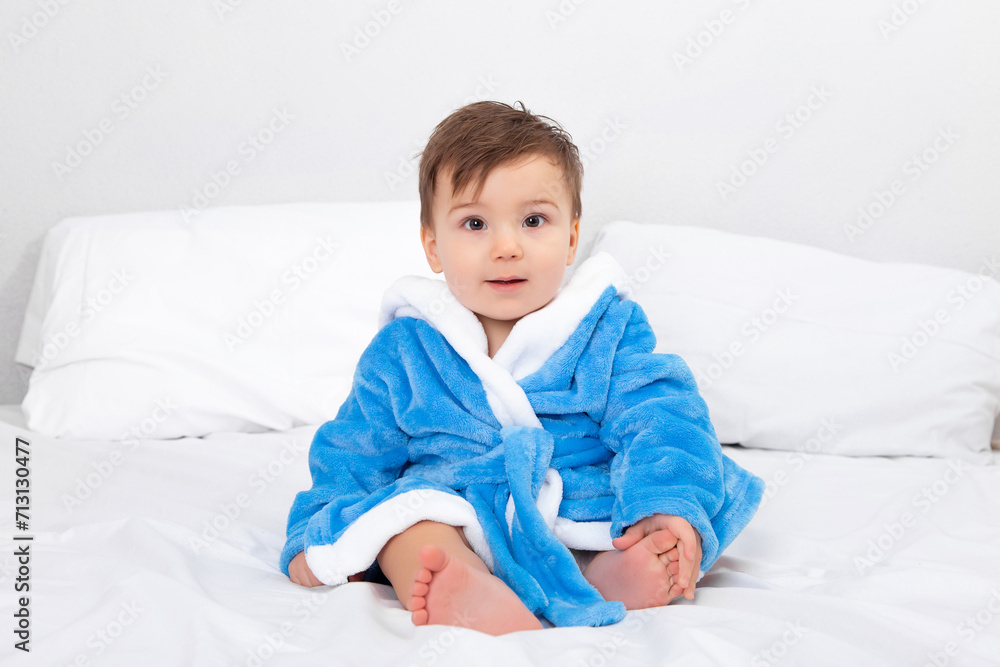 Baby in blue bathrobe, after bath, sitting on bed. Emotions, copy space. Baby in blue bathrobe, after bath, sitting on bed. Emotions, copy space.