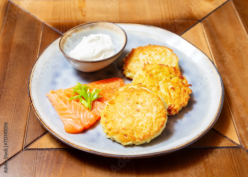 Potato pancakes and salmon with sour cream. On a wooden table.