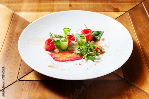 Red fish, salmon with cucumber and radish on a plate. Restaurant, cafe. On a wooden table.