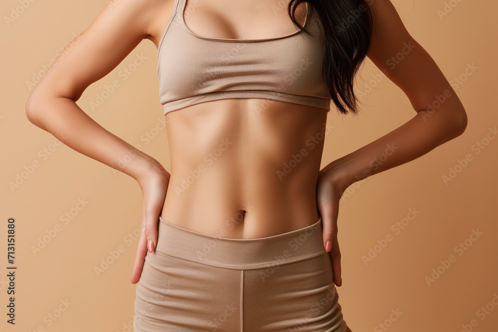 Naklejka premium Young woman with flat belly on beige background, closeup. healthy life concept. Plastic surgery concept.