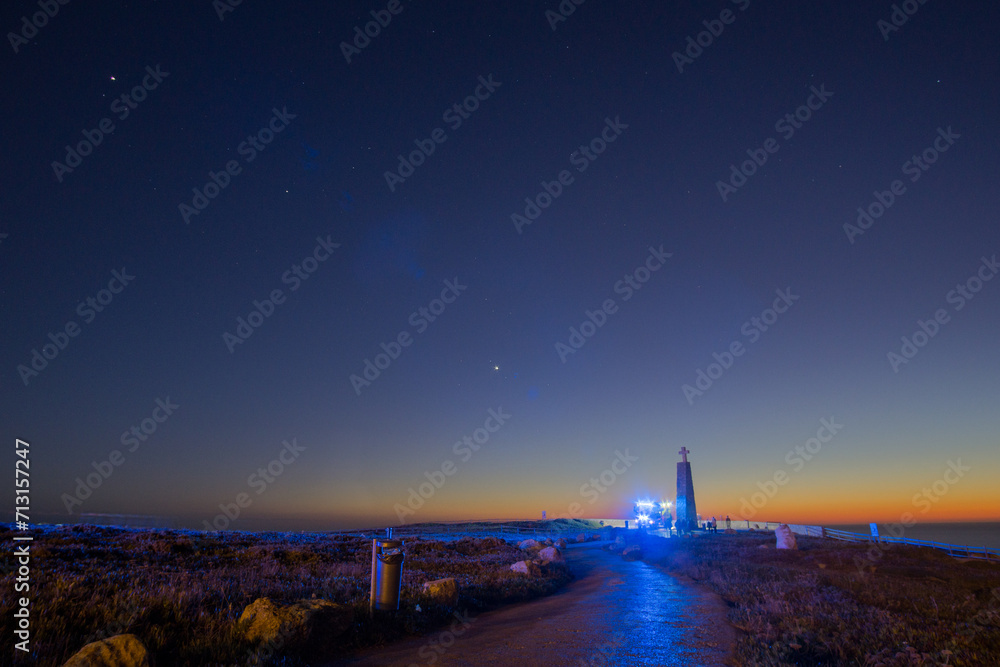 Path to the cross on a stone pillar at Cabo da Roca with fire truck with blue lights under the night sky, Sintra, Lisbon, Portugal