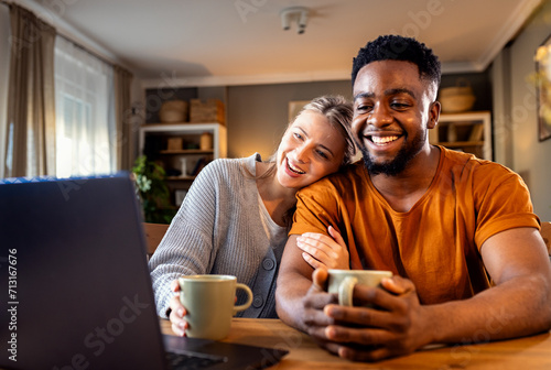 Cuadro en lienzo Smiling young mixed couple using a laptop while working on their home finances