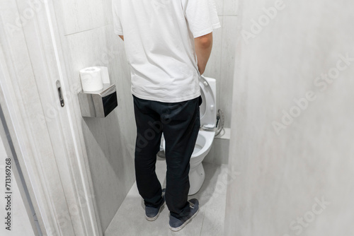 back view of Man Standing in Bathroom, urinating into a toilet.