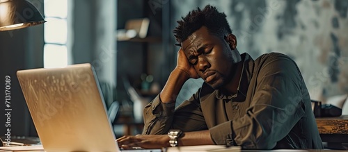 Stressed business man sitting at office workplace Tired and overworked black man Young african american exhausted men in stress working on laptop computer. Copy space image. Place for adding text photo