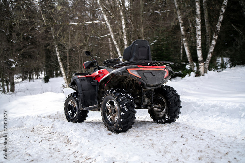 A red and black quad bike stands idle on a snow-covered trail, its presence contrasting with the serene, white winter landscape.