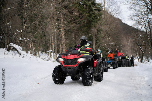 A man, equipped with cold-weather attire, confidently handles a red quad bike along a snowy path, surrounded by a wintry forest landscape.