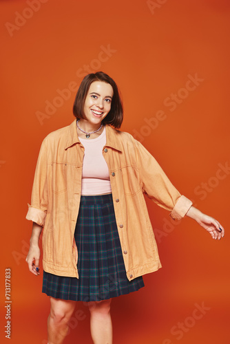 cheerful young woman with short hair looking at camera and smiling on orange background, joy