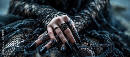 Hands with long black nails and gothic style finger rings lying on leg in fishnet tights. Copy space image. Place for adding text