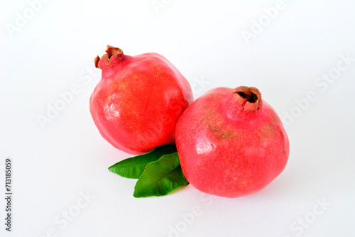 two red pomegranates with green leaves on white background