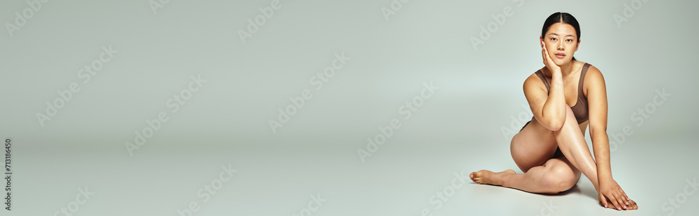 Obraz premium full length of young asian woman in underwear sitting with crossed legs on grey background, banner