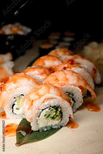 Side view of shrimp rolls coated in glossy sauce with cucumber filling and cream cheese on banana leaf