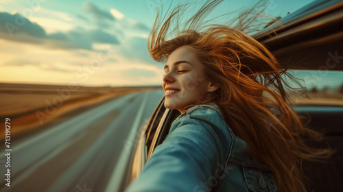 Adventure Time. A young woman leans out of a car window during a trip, feeling freedom. Travel, vacation or freedom concept.