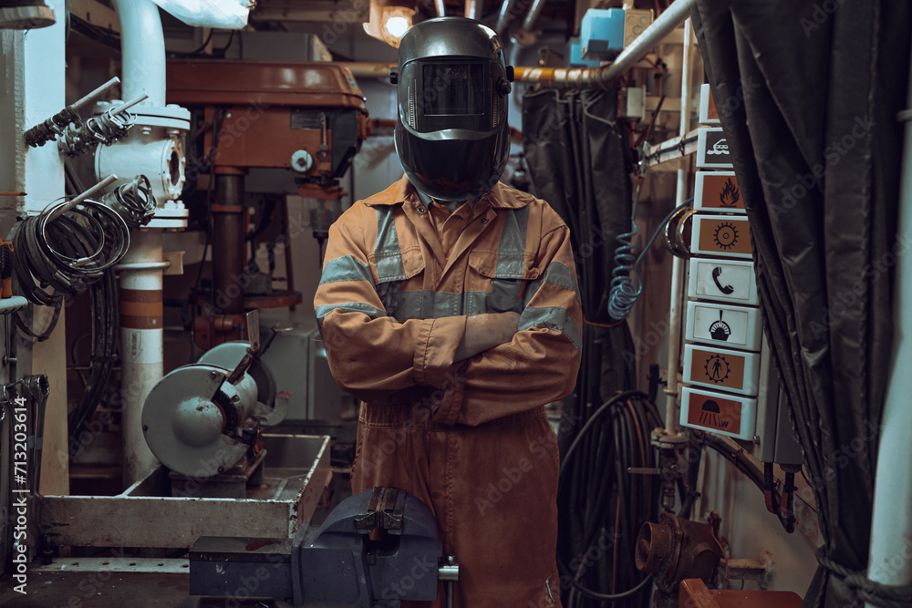 Standing portrait of welder wearing mask and orange coverall in workshop. Standing portrait of welder wearing mask and orange coverall in workshop.