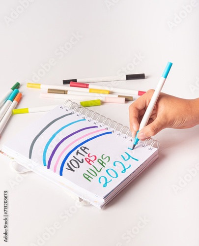 School supplies, teenager's hand writing back to school 2024 in Portuguese, white background, selective focus.