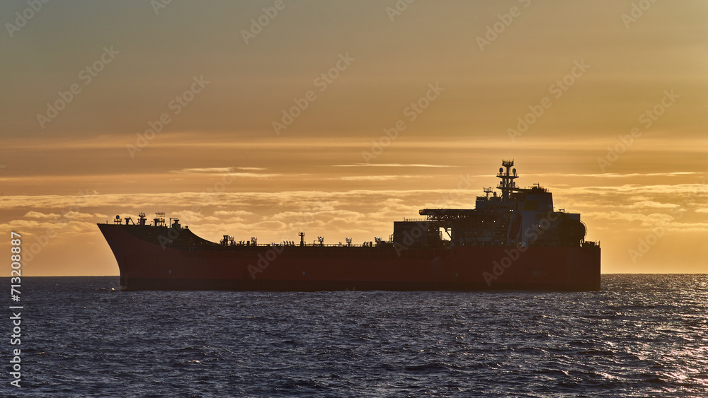 Beautiful ocean sunset, with golden sky, dark blue sea and silhouette of ship, oil tanker on the horizon.