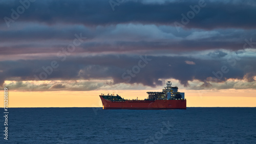 Beautiful ocean sunset, with colourful blue and golden sky, blue calm ocean and silhouette of ship on the horizon.