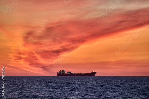 Panoramic view of colourful ocean sky , with red and orange clouds, dark sea and silhouette of a ship on the horizon.
