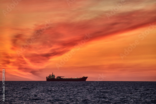 Beautiful ocean sunset , with colourful red and orange sky, dark sea and silhouette of ship on the horizon. © Igor Hotinsky