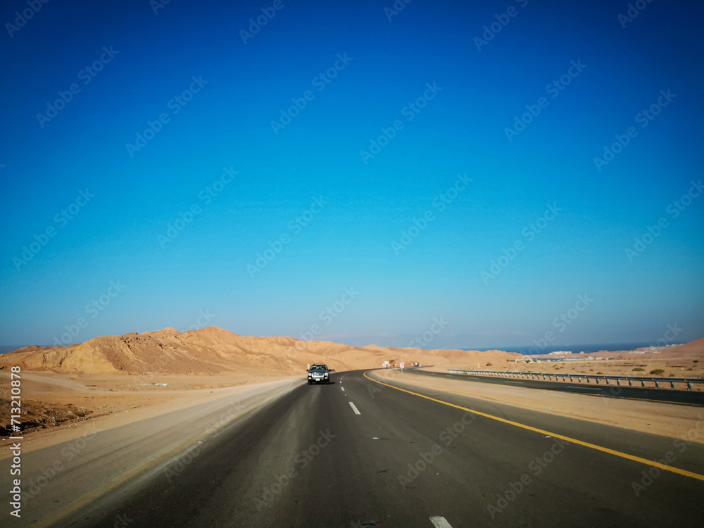 Highway through sand dunes. Highway in between mountains. Saudi Arabia's beautiful desert. Blue sky background 