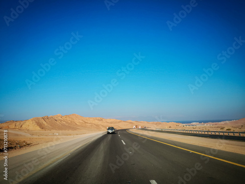 Highway through sand dunes. Highway in between mountains. Saudi Arabia's beautiful desert. Blue sky background  © Maaz