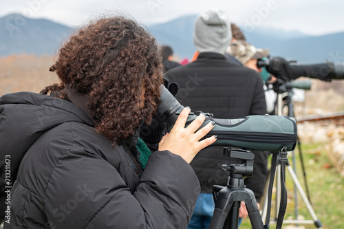 Woman birdwatching with a telescope by the lake in cold weather.